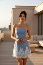 A woman modeling a strapless light blue denim mini dress with white lace trim at the hem, photographed against a plain white studio background.